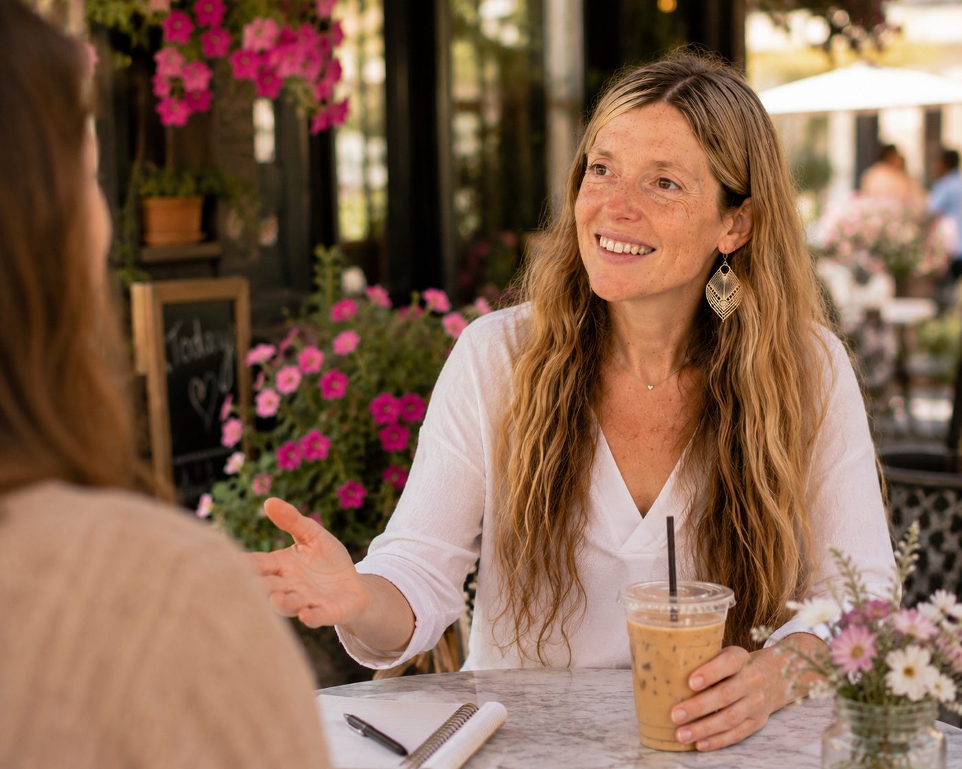 Dina Bright Yosef, RN, in warm conversation with a woman at a caf&eacute; table, notebook open between them